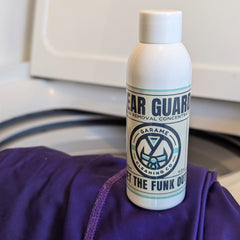 A single bottle of Gear Guard sits on top of a purple rash guard. The rash guard is draped over the edge of a washing machine.