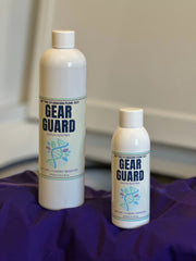 Two bottles of Gear Guard sits on top of a purple rash guard. The rash guard is draped over the edge of a washing machine.