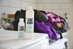 Two 'Gear Guard' bottles on a washing machine with workout gear in a gym bag in the background.
