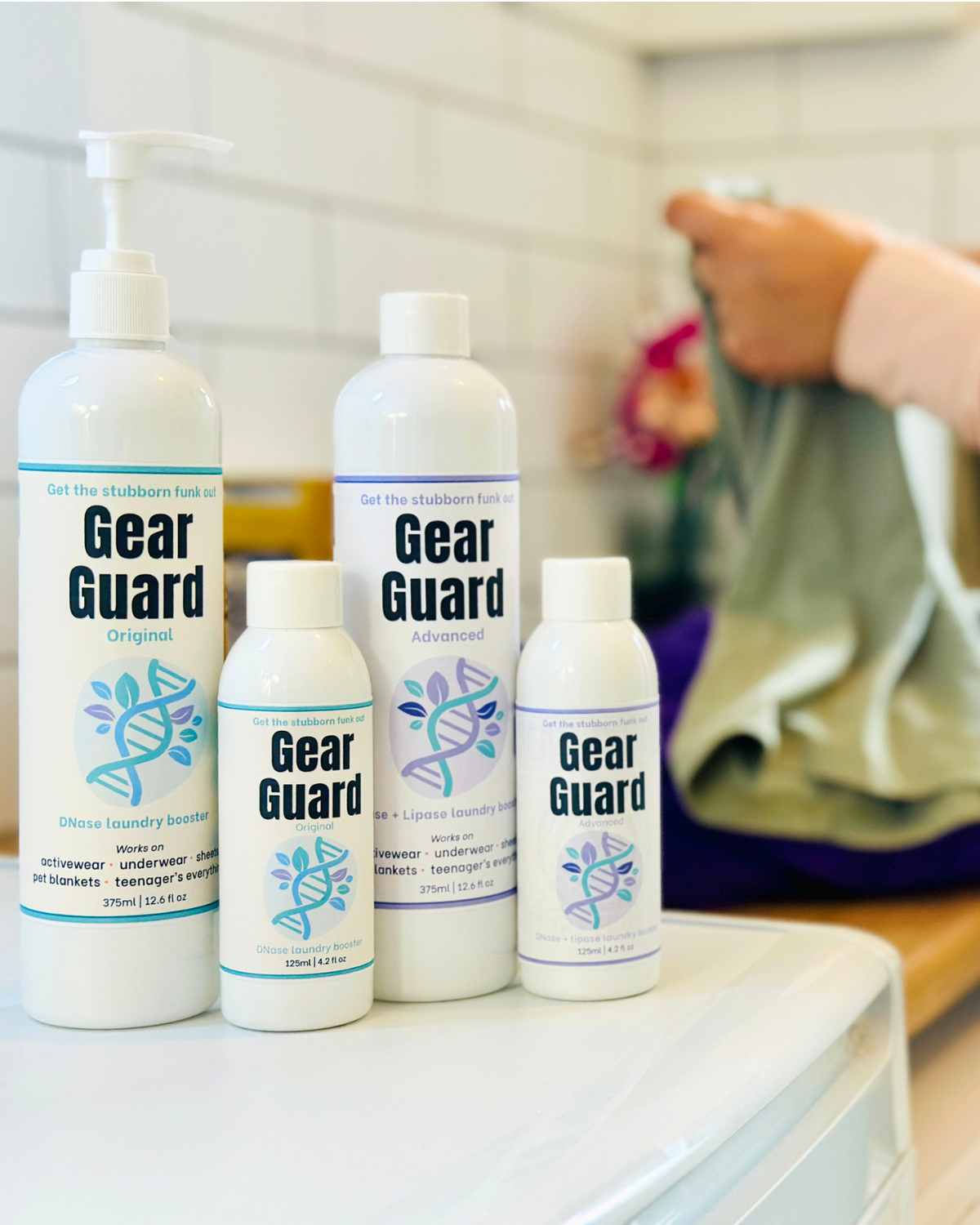 Gear Guard Oroginal and Advanced bottles of different sizes arranged on a white surface with a blurred laundry background.