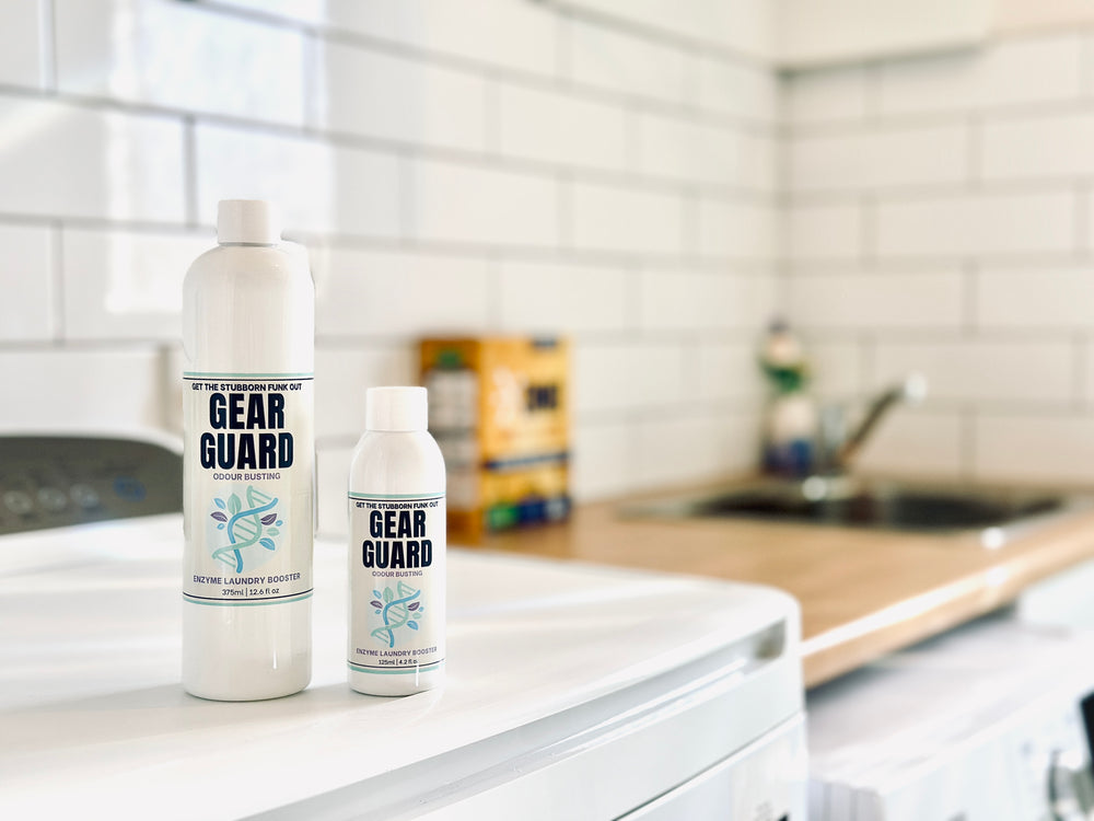 Two bottles of 'Gear Guard' on a washing machine with a blurred laundry room background