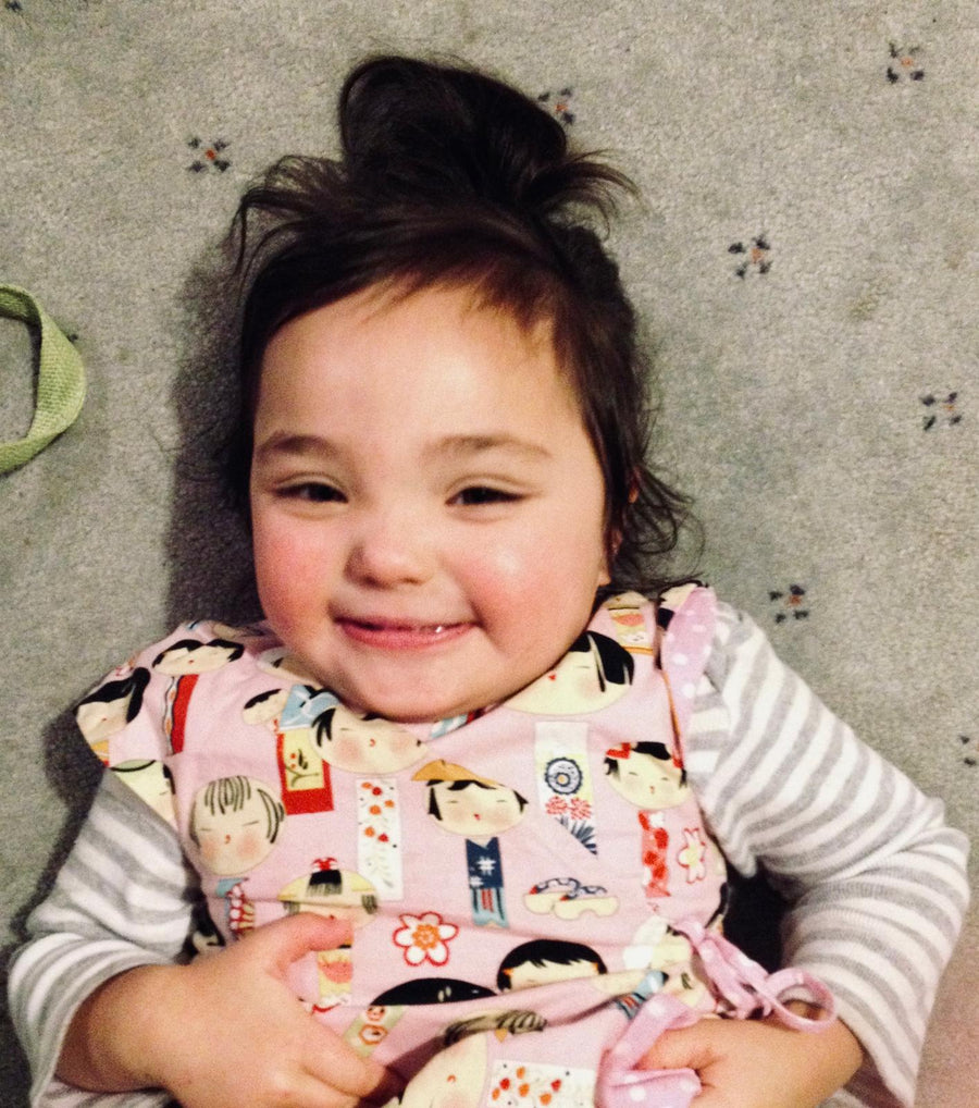 A young Kenzie smiling while lying on the carpet in a patterned pink outfit