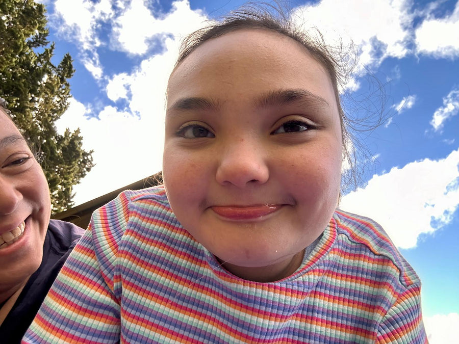 Kenzie smiles sweetly with a bit of drool, enjoying the moment outdoors under a bright blue sky with her Mum