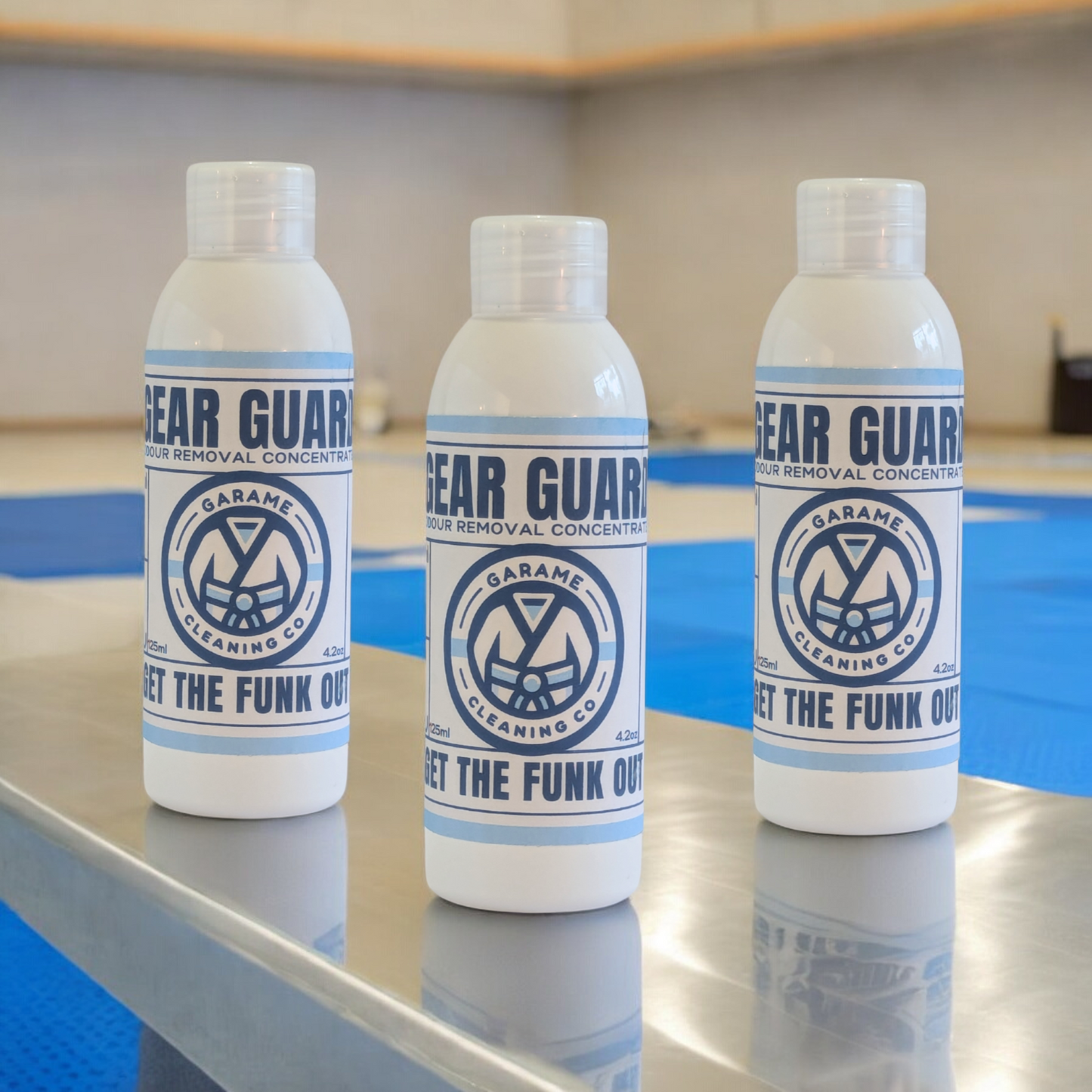 Three bottles of Gear Guard odour removal concentrate displayed side by side on a light grey surface, showcasing the mid-sized bundle option. The bottles are uniformly branded with a white bottle. The label has a sky blue border with dark blue writing. The Garame Cleaning Co logo is in the centre, Gear Guard written above and Get the funk out below.