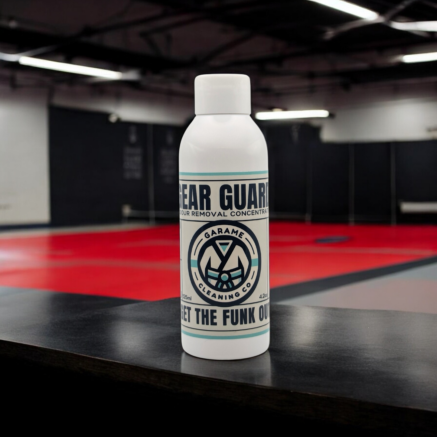 A single bottle of Gear Guard odour removal concentrate on a wooden table in a martial arts gym setting, prominently displaying the Garame Cleaning Co logo and the slogan 'GET THE FUNK OUT.' The bottle is white with a label  that has a light blue border, dark blue text and a simple, clean design.