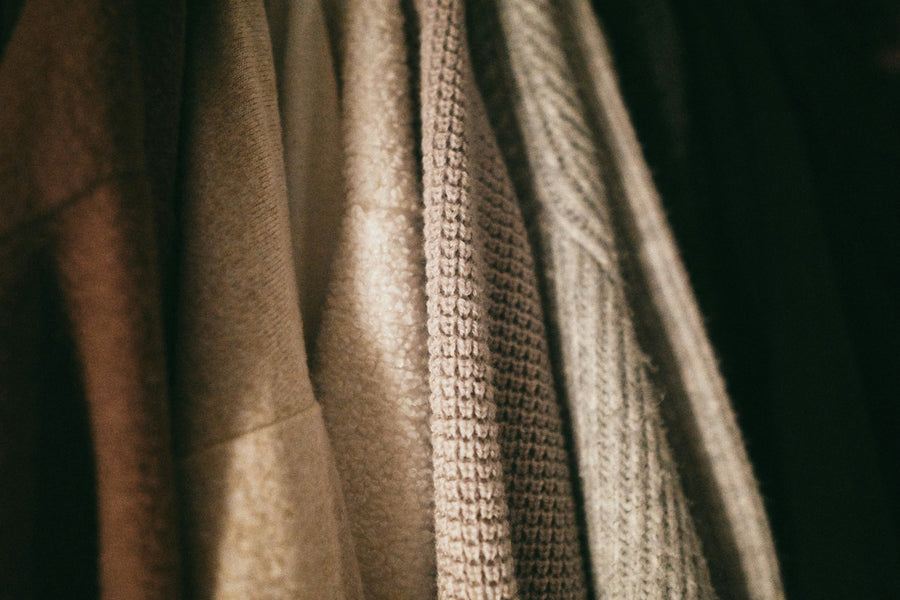 Natural fibre jumpers and coats hang in a wardrobe. Photo by Haley Truong on Unsplash.